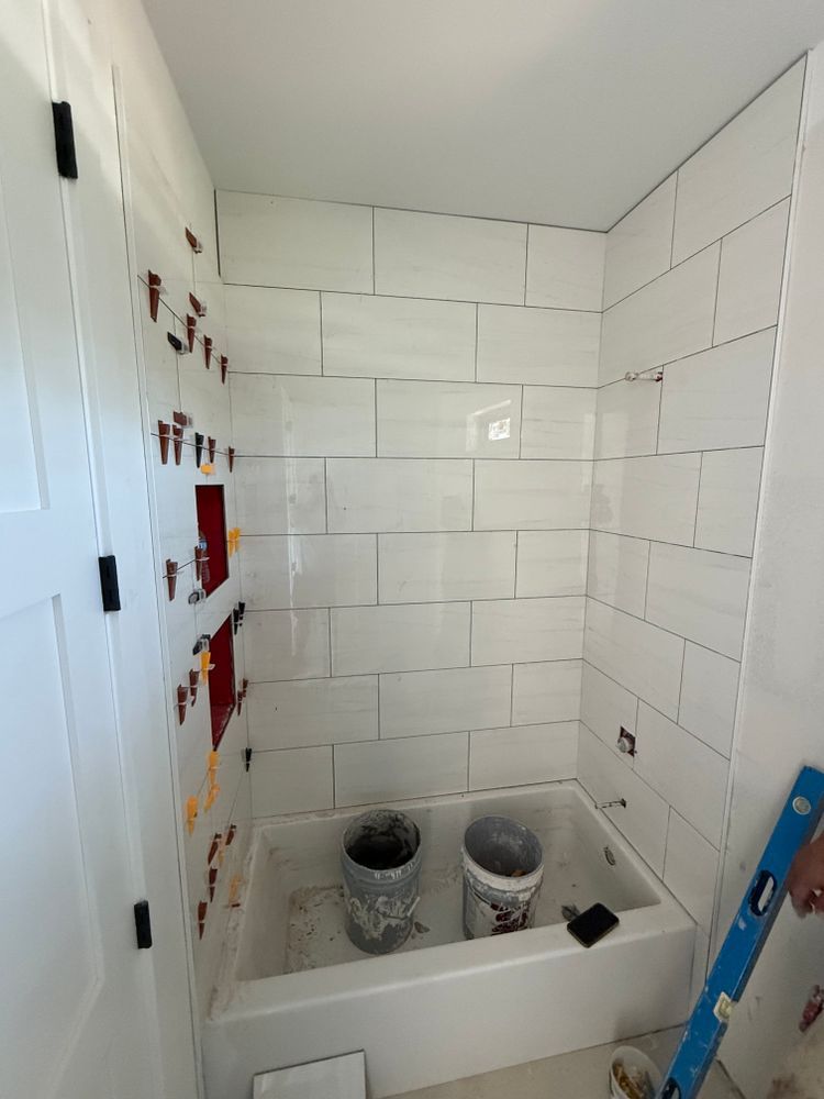 Partially tiled shower being renovated, with two buckets and tools on a white bathtub floor