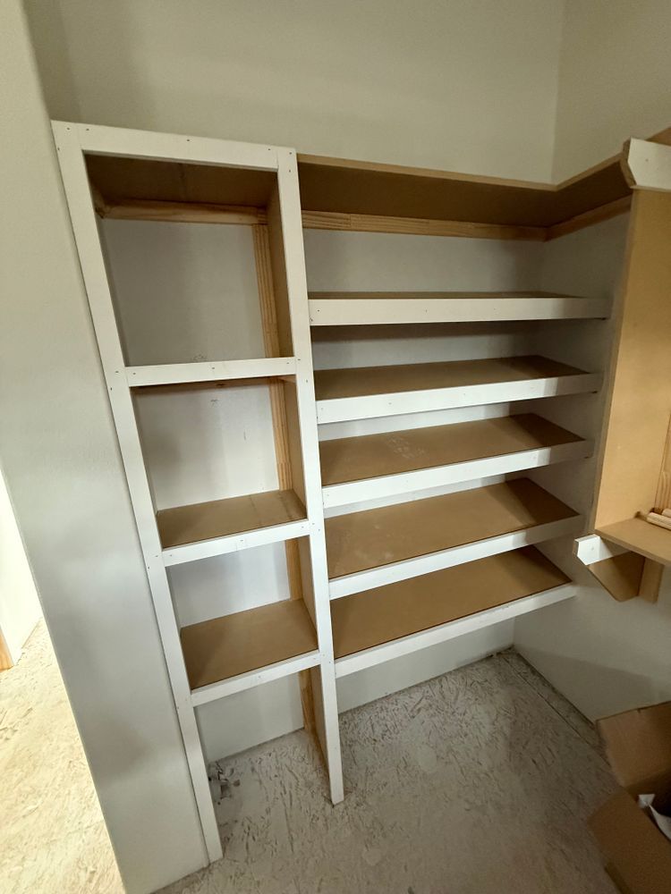 Empty built-in closet with white shelves and hanging space, beige walls, and carpeted floor