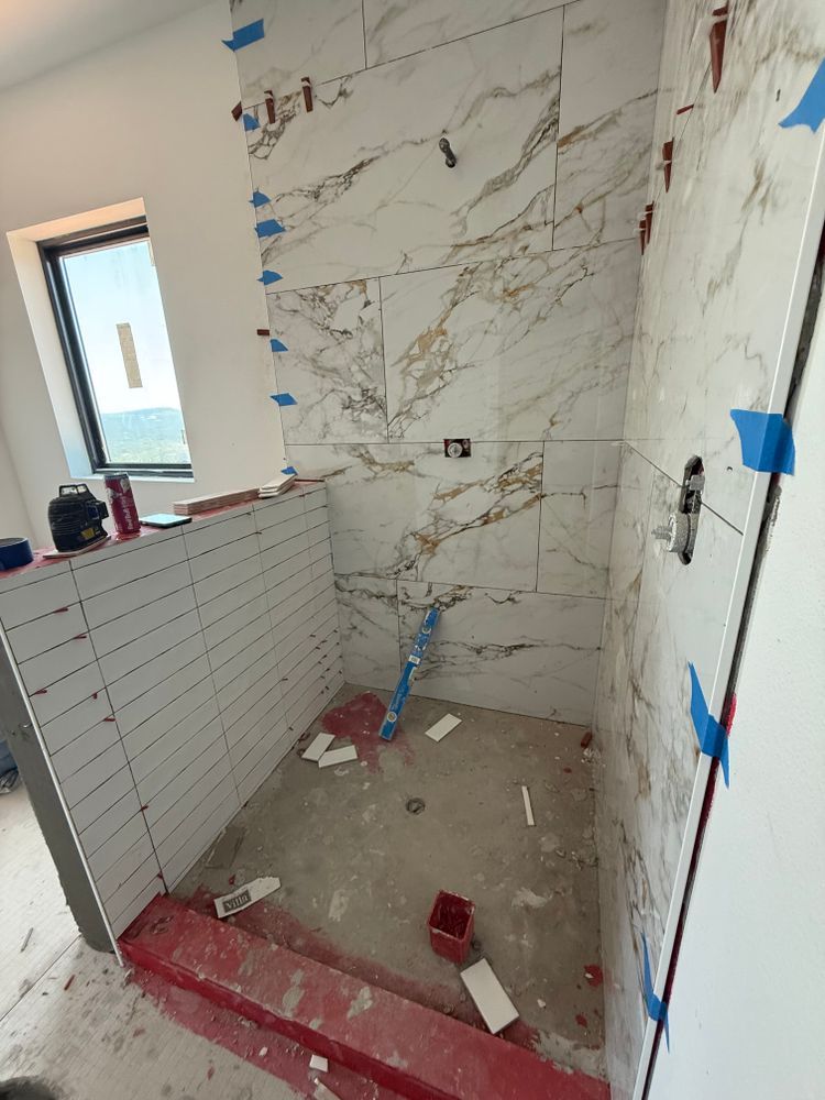 Small bathroom shower under renovation with white tile, marble-pattern wall, blue tape, and construction debris