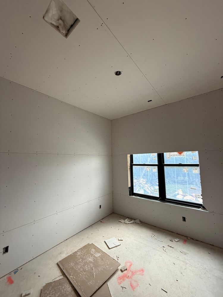 Empty unfinished room with gray walls, white floor, exposed ceiling fixtures, and a window on the right.