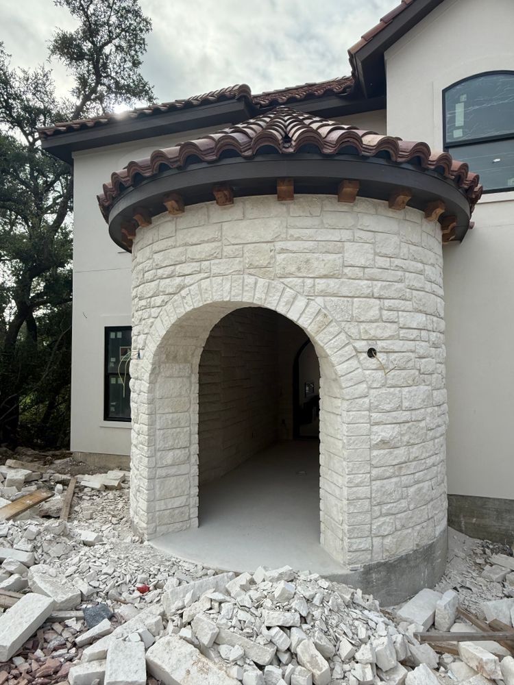 Stone-front home entrance under construction with arched doorway and debris in front