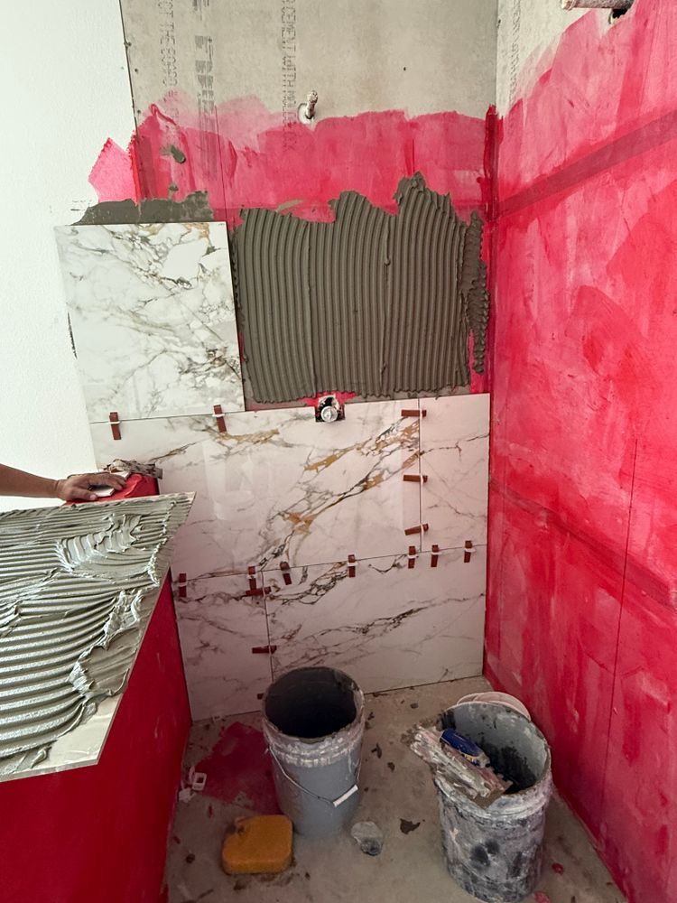 Partially tiled bathroom wall with pink paint, exposed rough plaster, and buckets on the floor