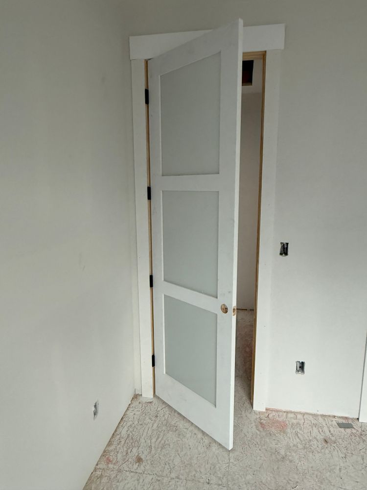 Partially open white interior door in an unfinished room with bare walls and carpet.