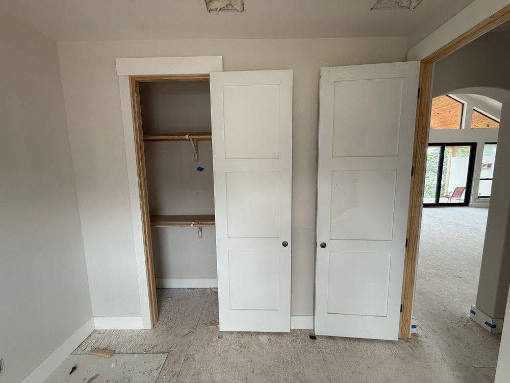 Empty room with open white closet doors, beige carpet, and arched doorway into another room