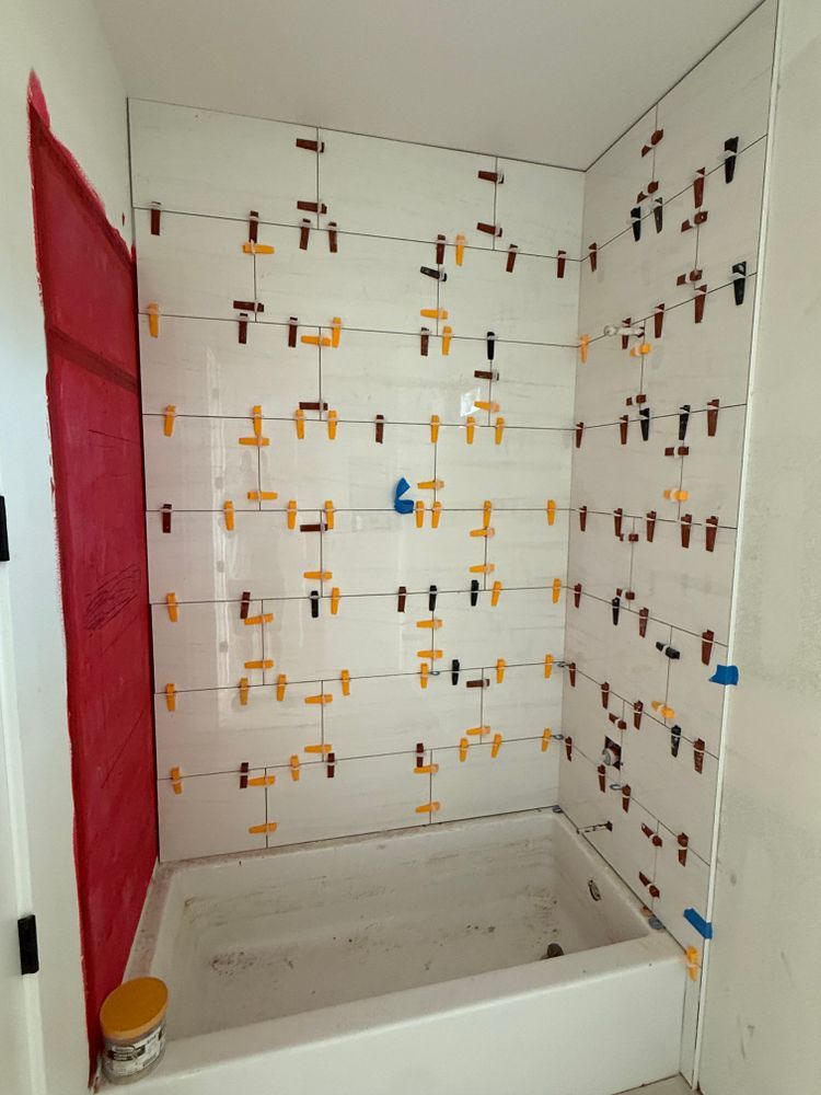 Bathroom shower stall under renovation with tile spacers on white walls and a red plastic sheet on the left.