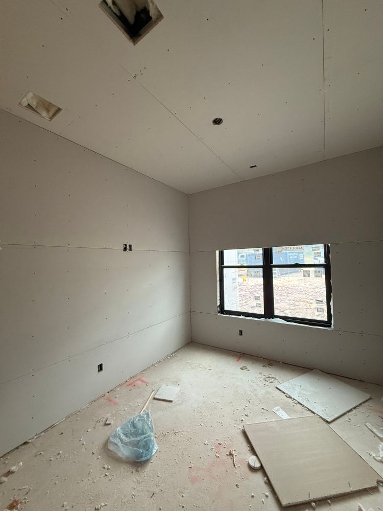 Empty unfinished room with bare walls, debris on the floor, and a window letting in light.