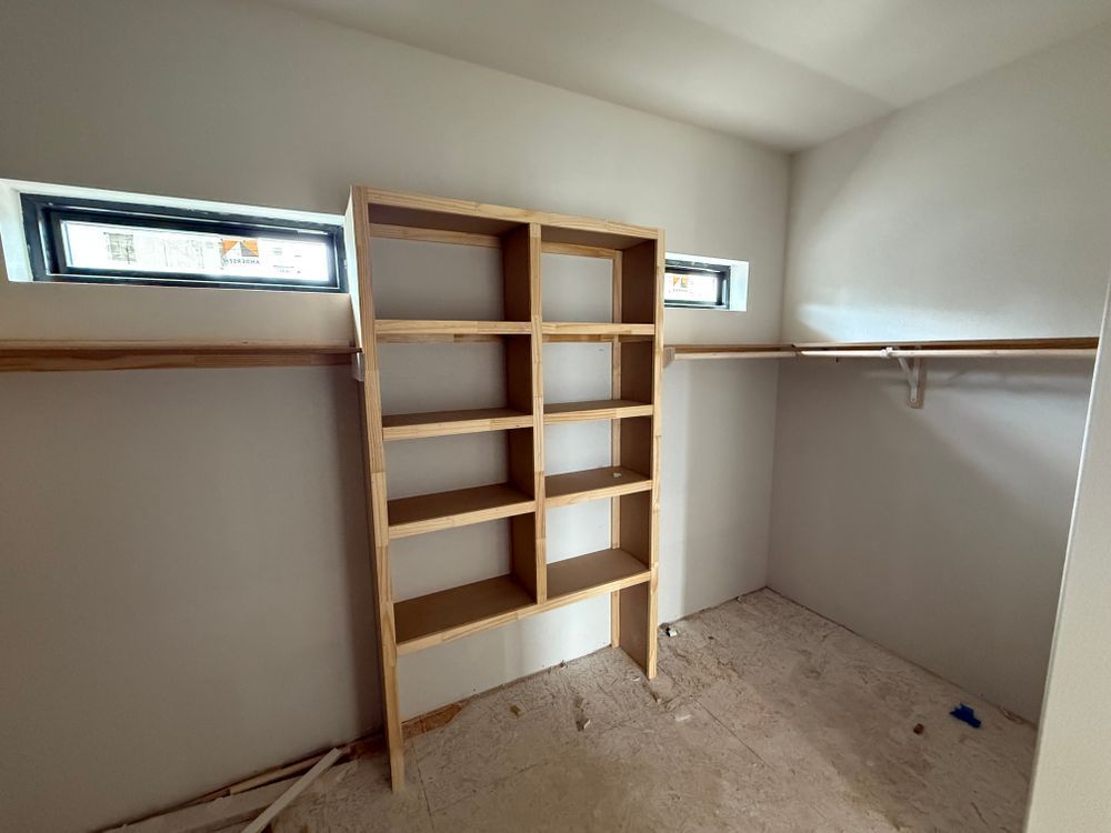 Empty walk-in closet with built-in wooden shelves, hanging rods, and small windows.