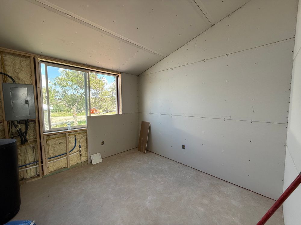 Empty unfinished room with white walls, carpet, and a large window showing trees outside.