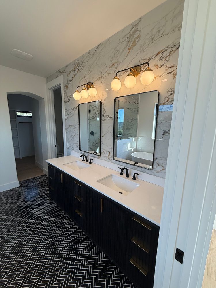 Modern double-sink bathroom with marble wall, black cabinetry, and chevron tile floor.