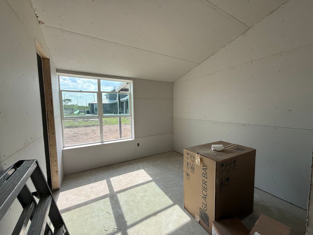 Empty unfinished room with white drywall, window light, and a cardboard box on the floor.