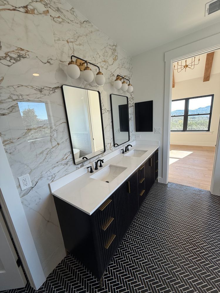 Modern bathroom vanity with double sinks, marble-look wall, black cabinets, and patterned floor tiles