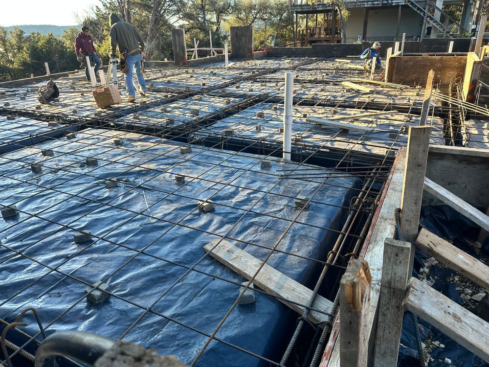 Construction site with workers installing rebar and black plastic sheeting for a concrete slab foundation