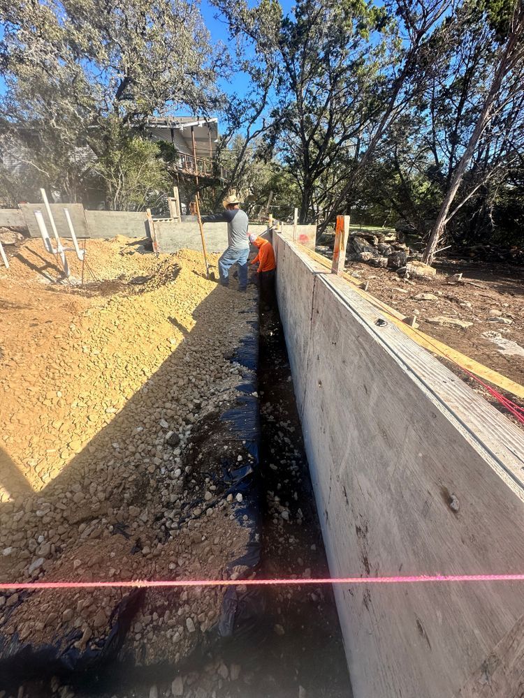 Trenched construction site with concrete retaining walls, dirt, and a worker in a red shirt.