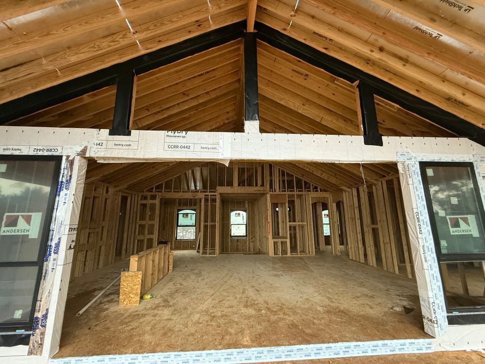 Interior of an unfinished wooden house with exposed beams and open framing beneath a vaulted roof.