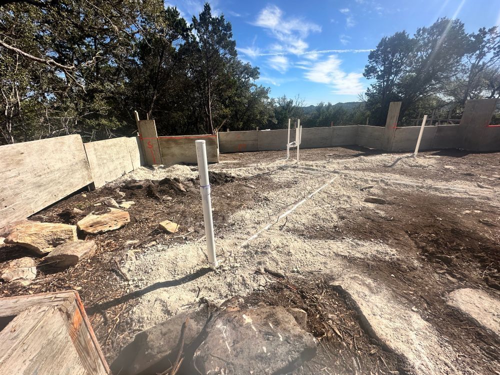 Empty construction site with concrete foundation walls, utility posts, and trees under a sunny sky