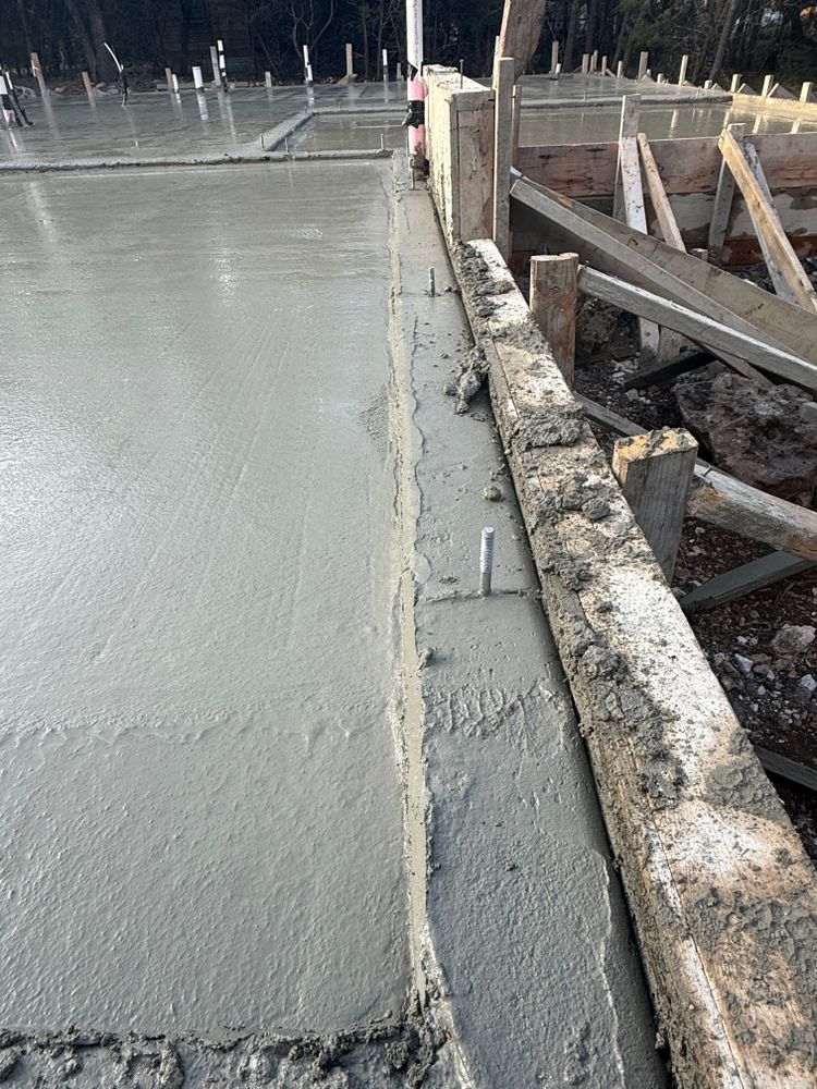 Fresh concrete slab being poured beside a weathered wooden form on a construction site.