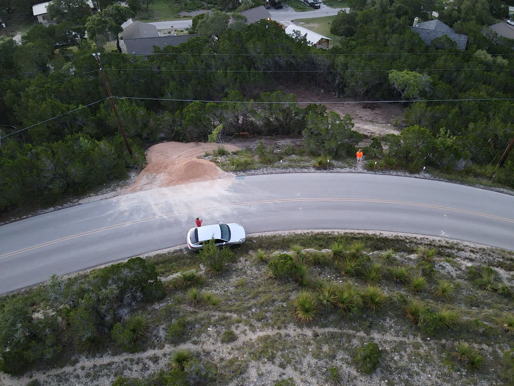 Aerial view of a winding road with a white car and two people near a curve in a wooded area