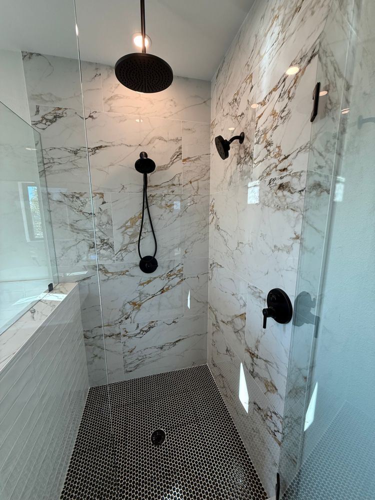 Modern tiled shower with black fixtures, marble-look walls, and mosaic floor