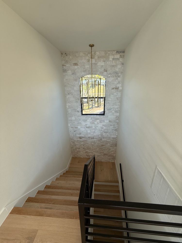 Stairwell with wooden steps, black railing, and a small window at the landing in a white hallway.