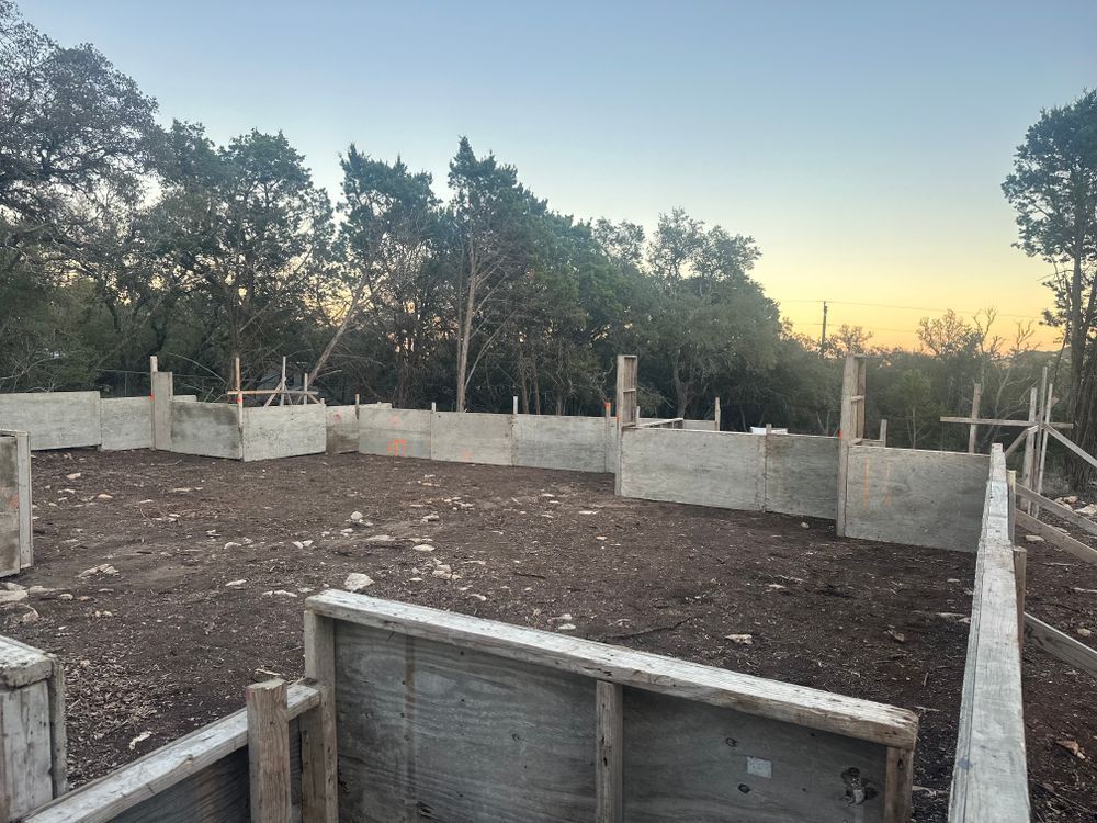 Partially built concrete foundation at sunset, surrounded by trees and wooden forms
