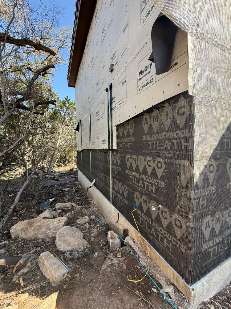 Partially sided house under construction beside rocky ground and trees