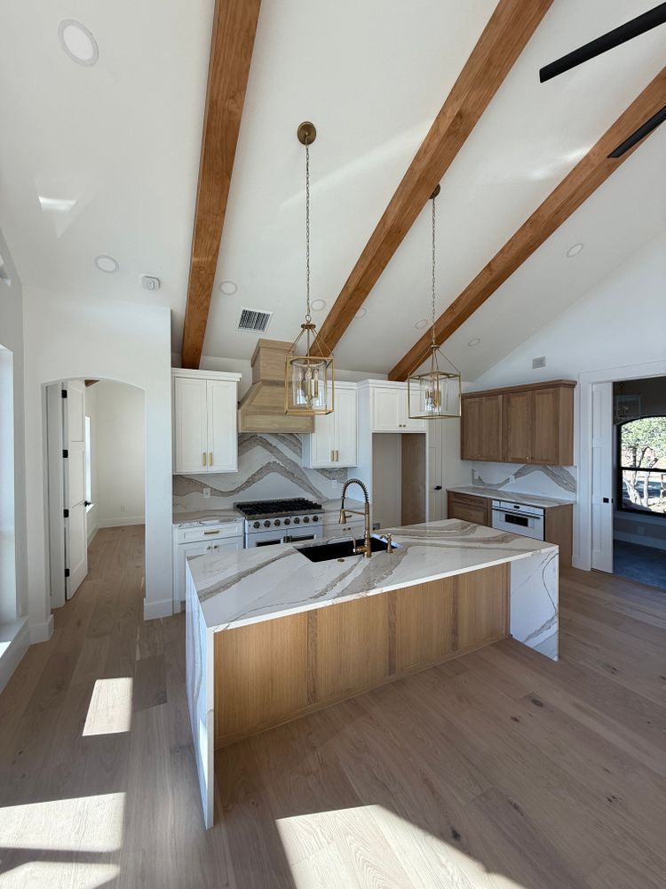 Bright modern kitchen with white cabinets, wood beams, and a marble island in an open living space