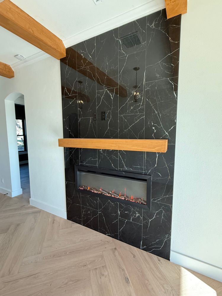 Modern living room fireplace with black tile, wood mantel, and herringbone floor to ceiling ceiling beams