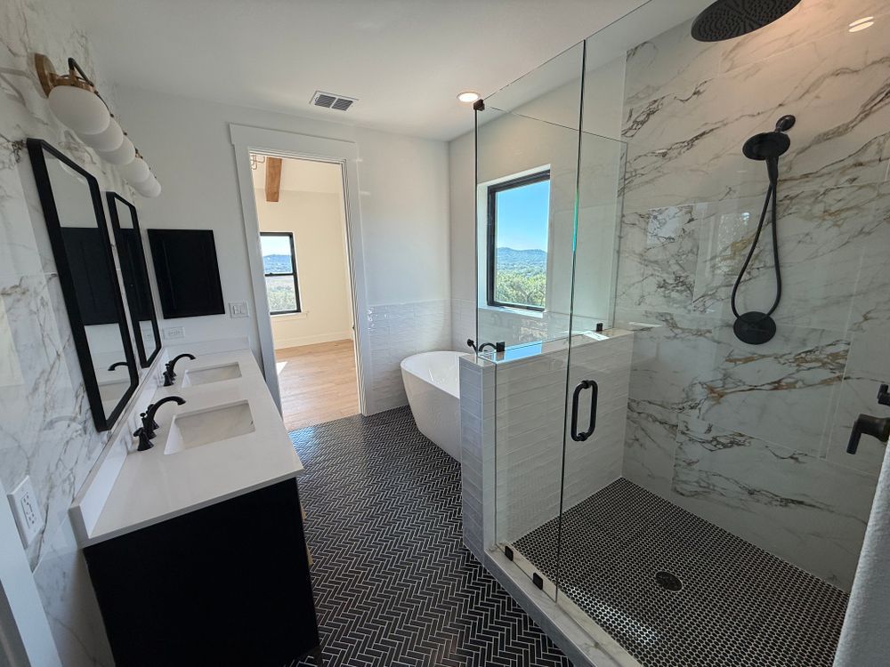 Modern bathroom with marble shower, black fixtures, white vanity, and patterned floor tile