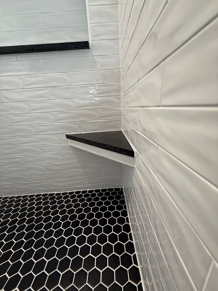 White tiled corner shower with black hexagon floor and a dark bench shelf
