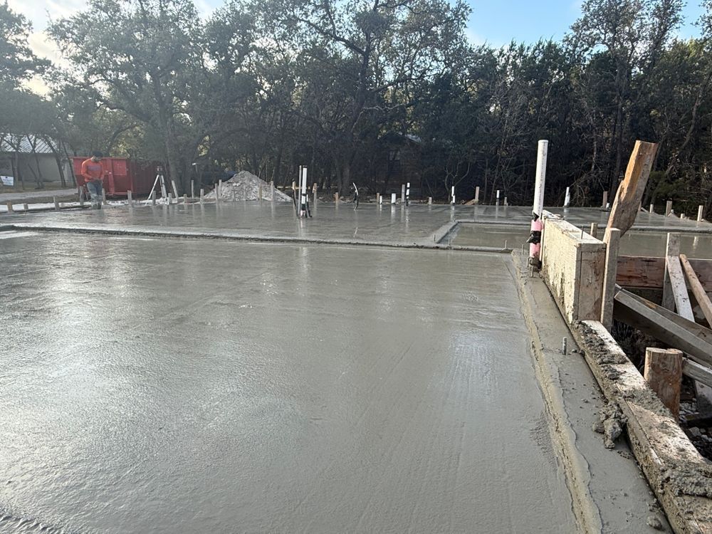 Freshly poured concrete slab at a construction site with forms, rebar, and trees in the background
