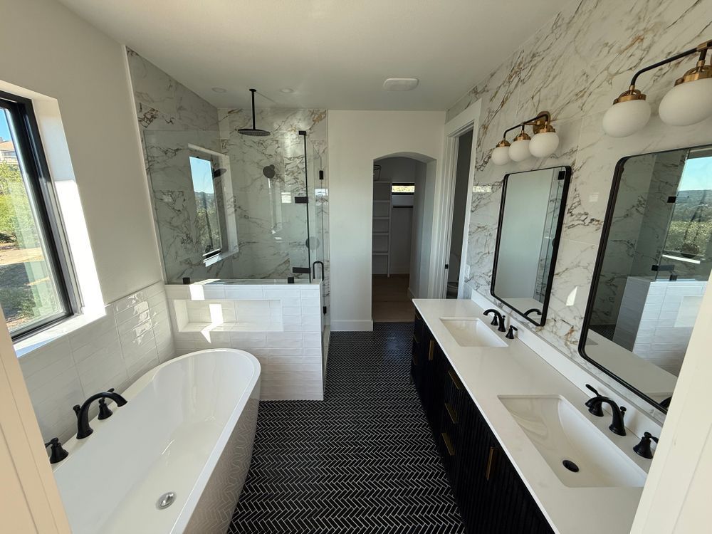 Bright white bathroom with black accents, freestanding tub, double sinks, large mirrors, and walk-in shower.