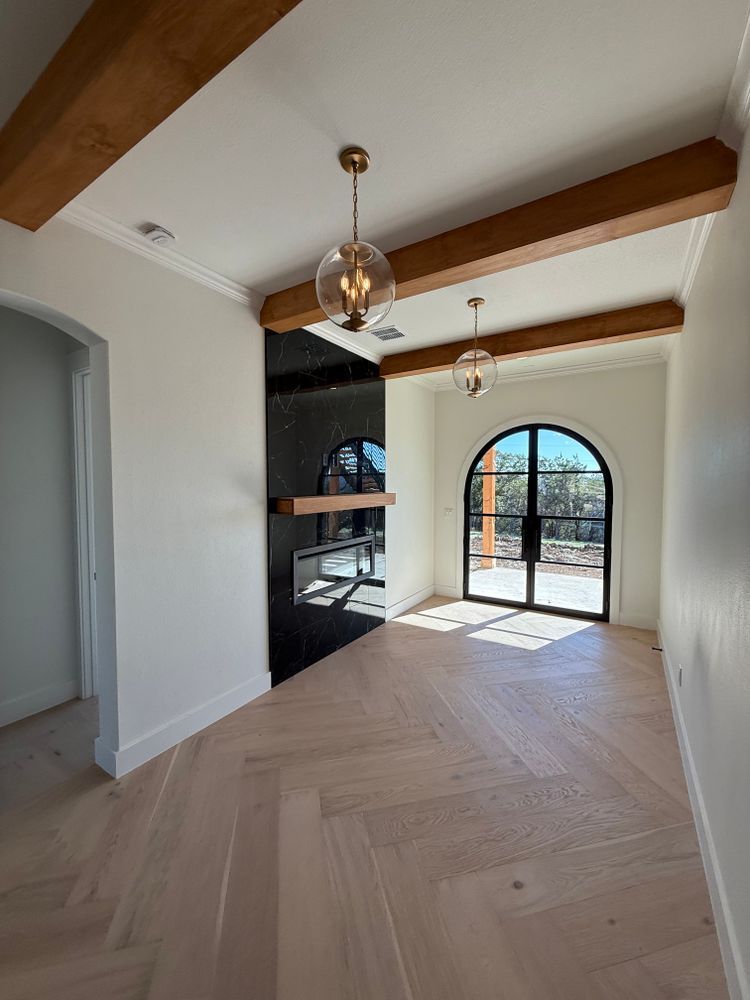 Bright empty room with wood beams, herringbone floor, and arched glass doors to a patio