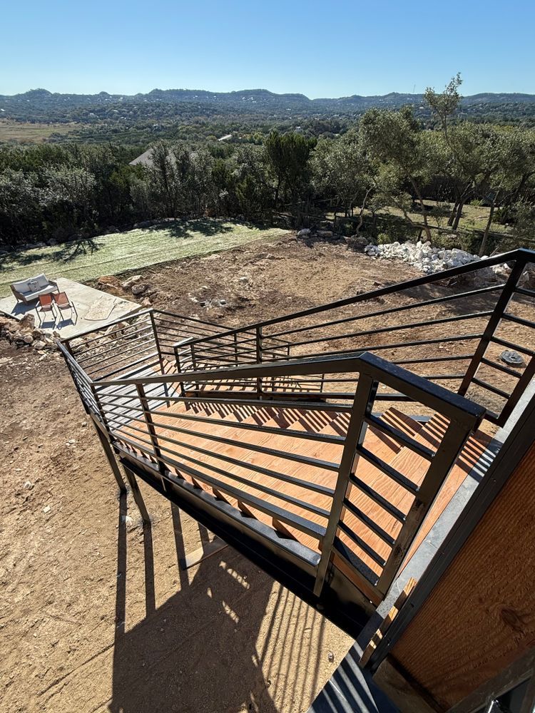 Rooftop stairs with black railing overlooking a dry, wooded landscape and distant hills