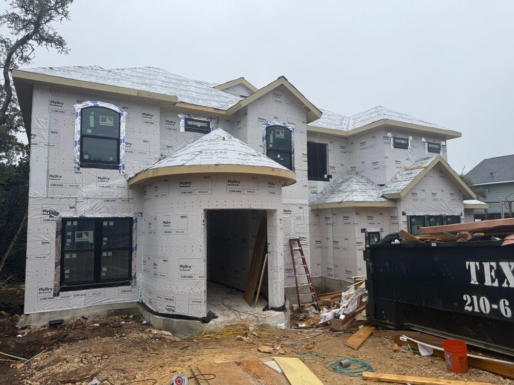 Unfinished two-story white brick house under construction with roof trusses and a dumpster in front.