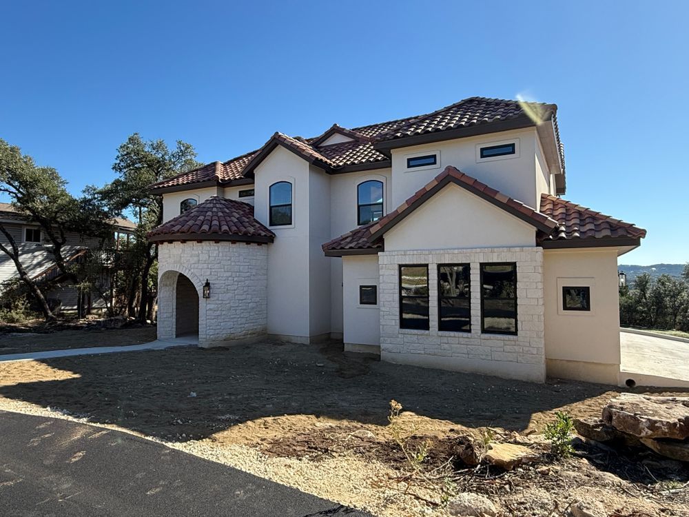 Two-story beige stucco house with red-tiled roof on a sunny, bare lot