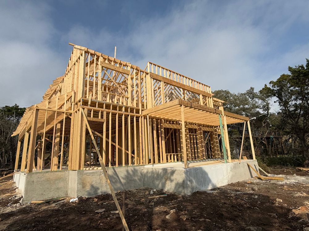 Partially framed house under construction on a concrete foundation under a cloudy sky