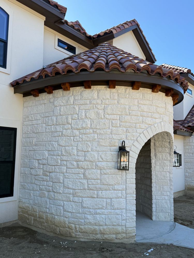 White stucco house entry with arched doorway, stone walls, and red-tiled roofline.