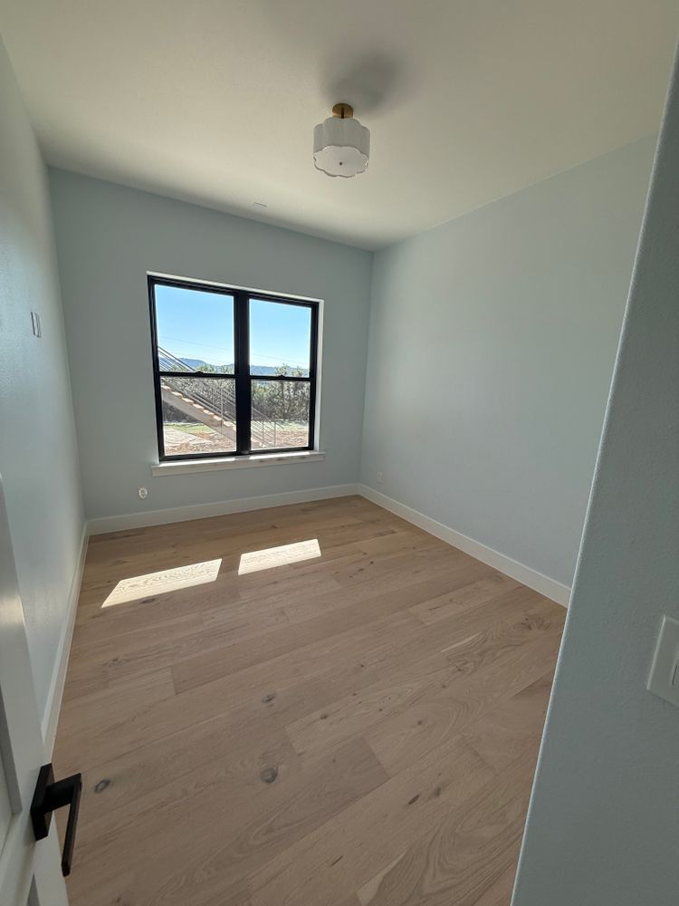 Empty light-blue room with wood floors and a window letting in sunlight.
