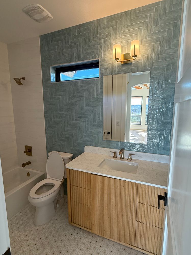 Accessible bathroom with white toilet, wood vanity, blue tiled accent wall, and wall sconces.
