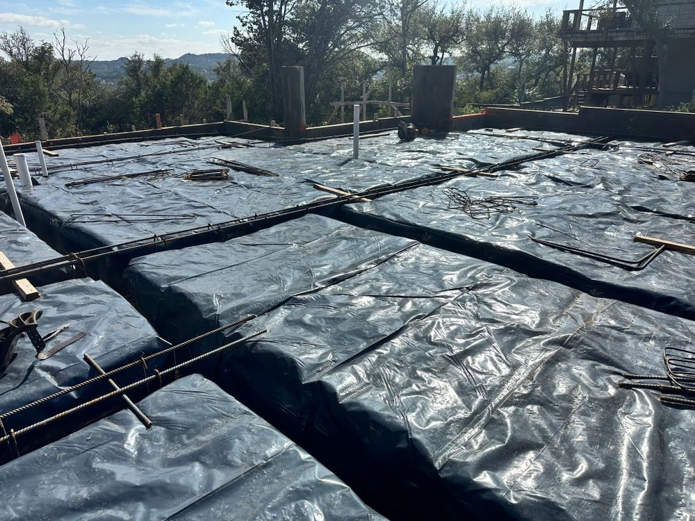 Black plastic ground cover stretched over a garden plot with pipes and posts in the background.