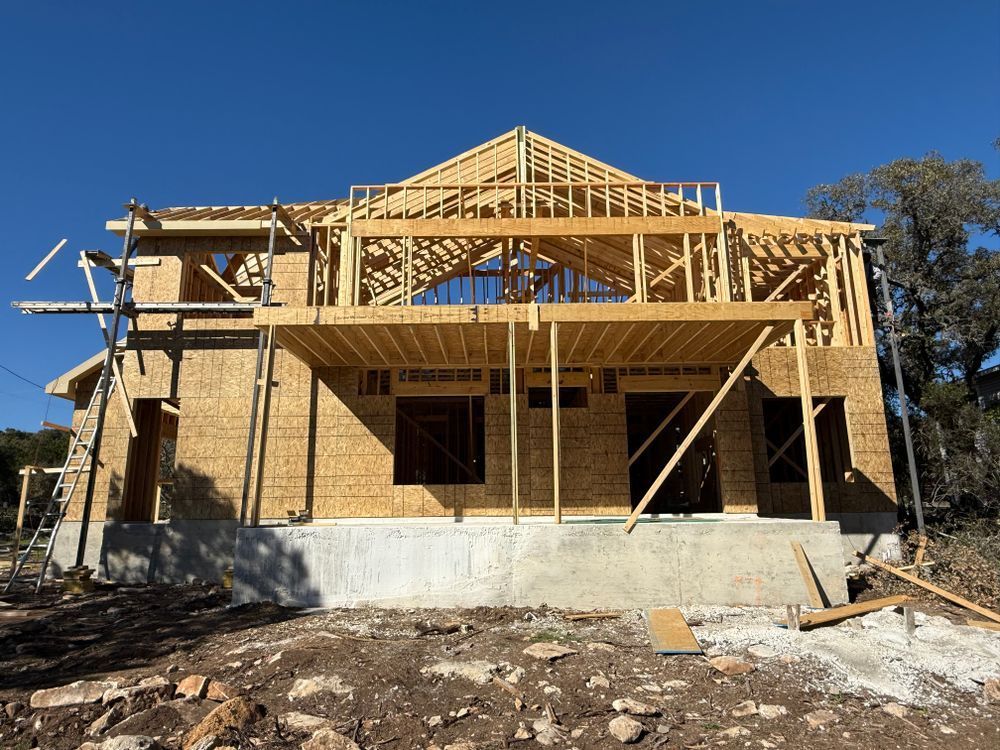 Partially built wooden house framed on a concrete foundation under a clear blue sky