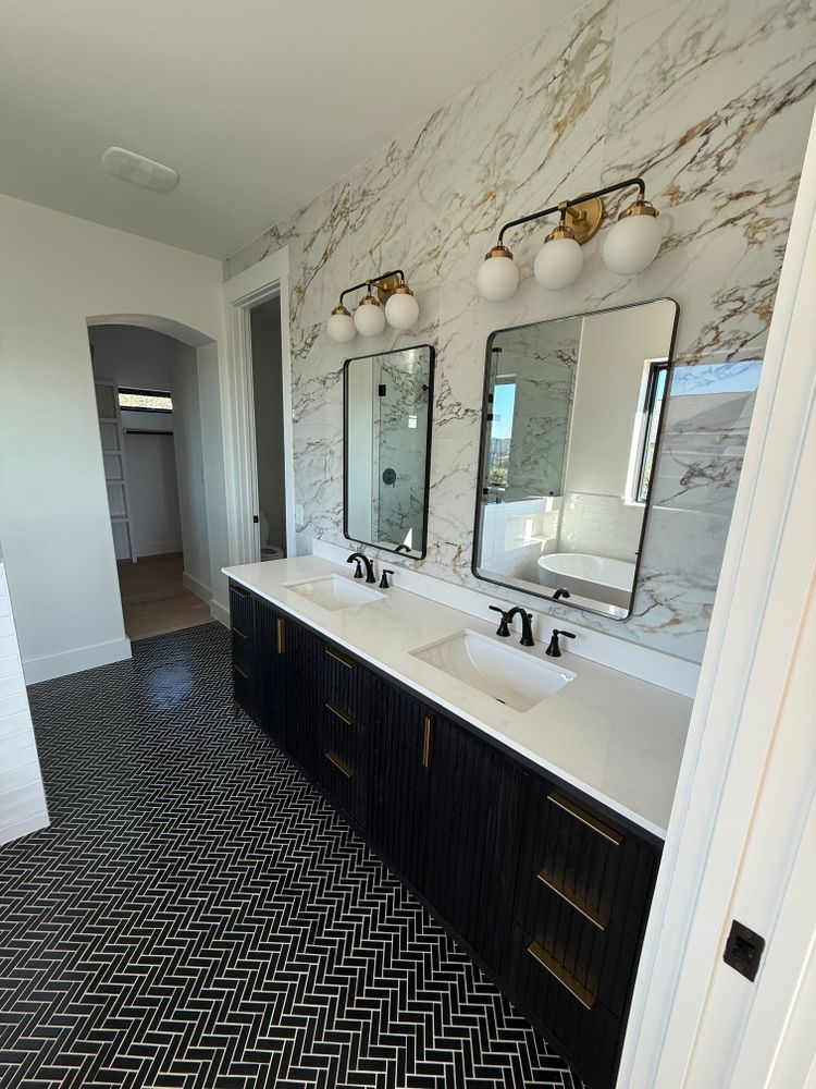 Modern bathroom vanity with two mirrors, black cabinets, white countertop, and patterned tile floor.
