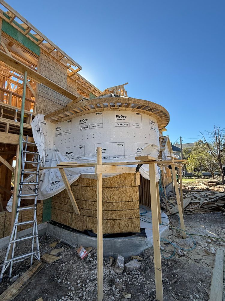 Partially built round house under construction, wrapped in white sheathing beside scaffolding and ladders