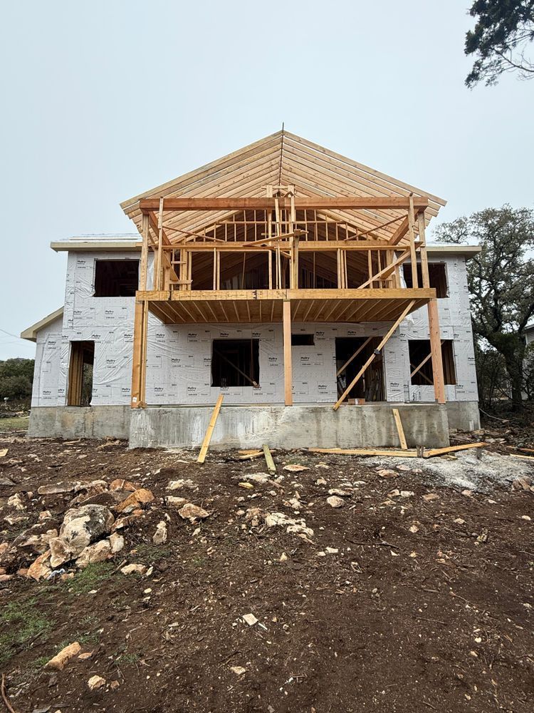 Partially built two-story house with exposed wooden roof framing and stone exterior under construction
