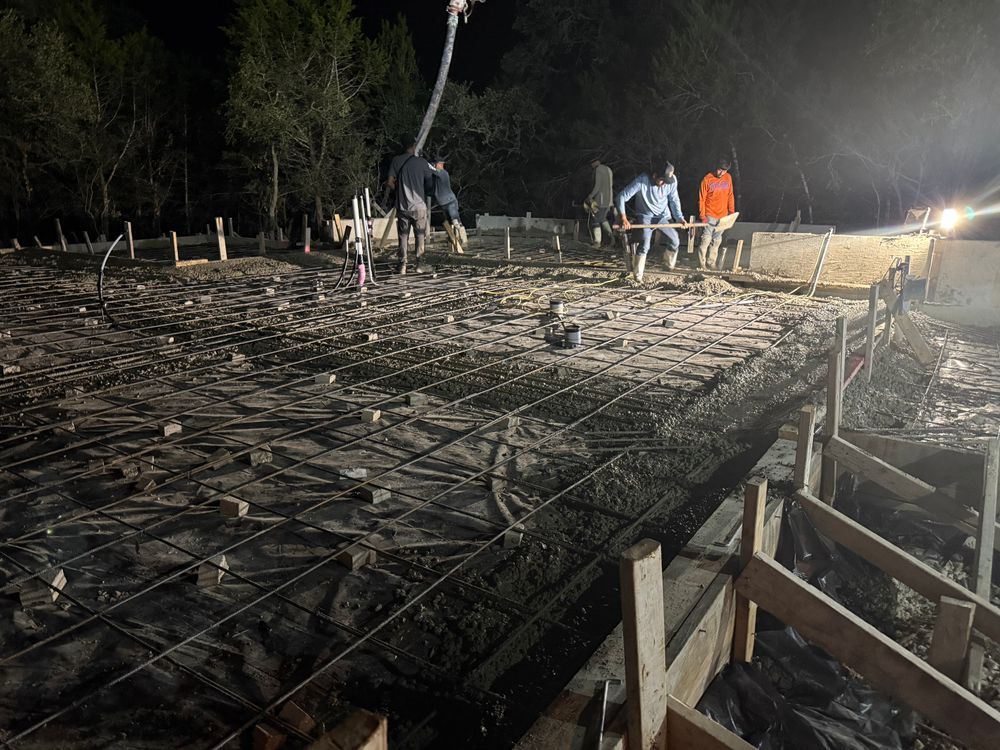 Nighttime construction site with workers pouring concrete over a rebar foundation frame
