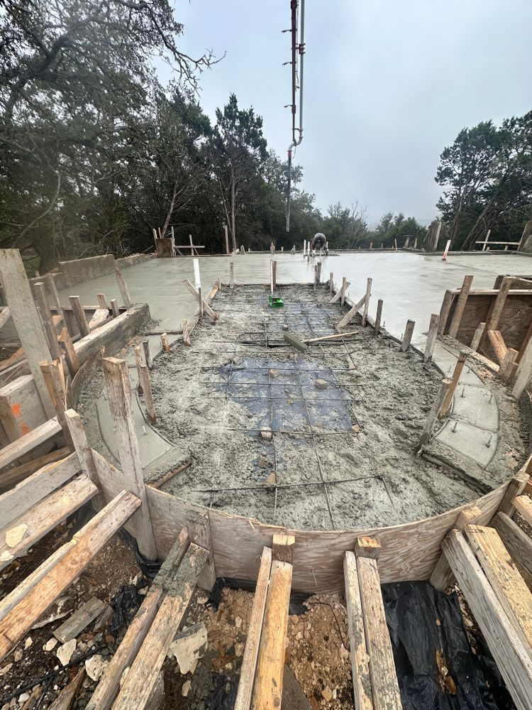 Concrete foundation under construction with wooden forms, rebar, and muddy worksite around a curved slab.