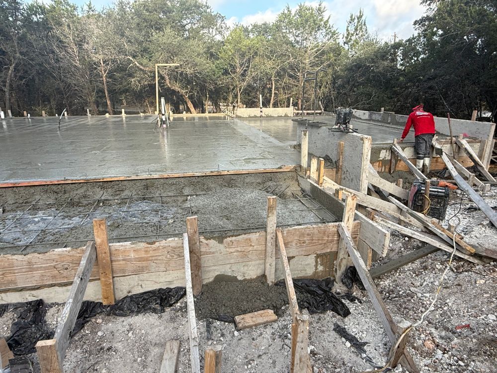 Construction site with a concrete foundation and workers pouring concrete beside a wooded area