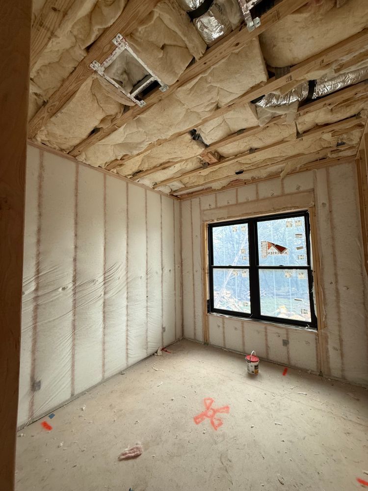 Unfinished room with insulated walls and ceiling, exposed beams, and a window letting in daylight.