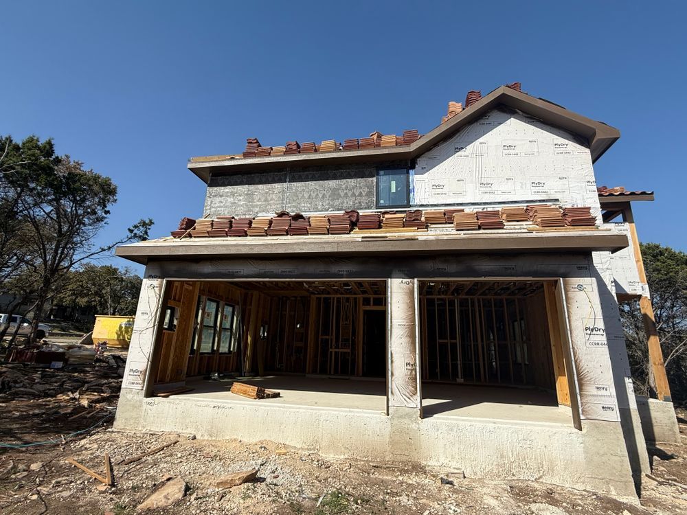 Two-story house under construction with exposed brick, large front porch, and unfinished walls under a clear blue sky
