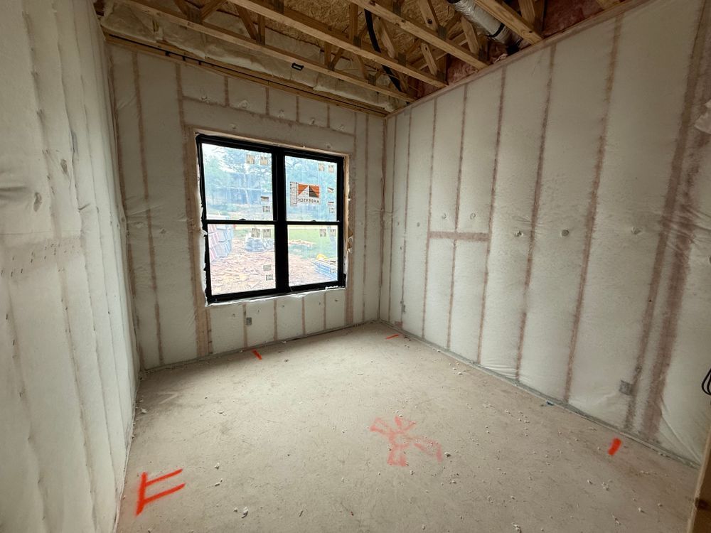 Unfinished room with insulated walls, exposed rafters, and a small window letting in daylight.